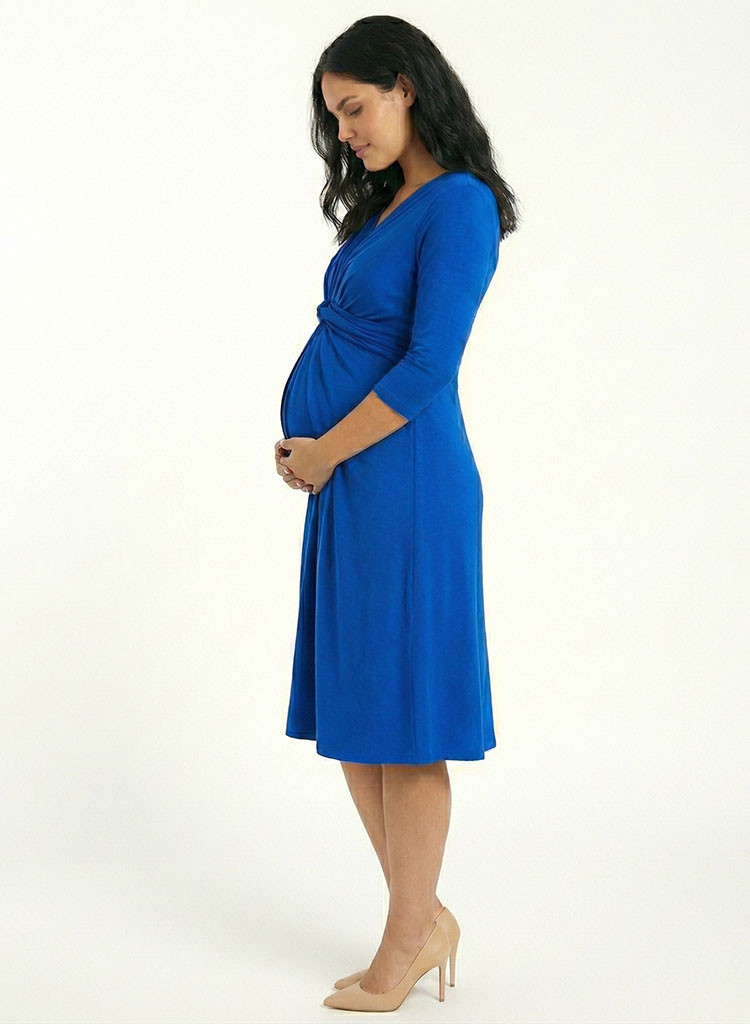 Mujer embarazada de perfil luciendo vestido materno midi azul rey, mostrando el ajuste cómodo y drapeado sobre la barriga